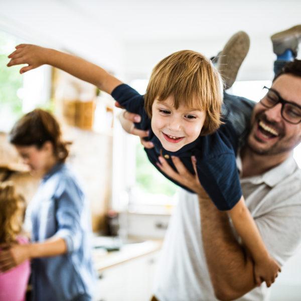 Happy little boy having fun with his father at home with the mom and daughter in the background