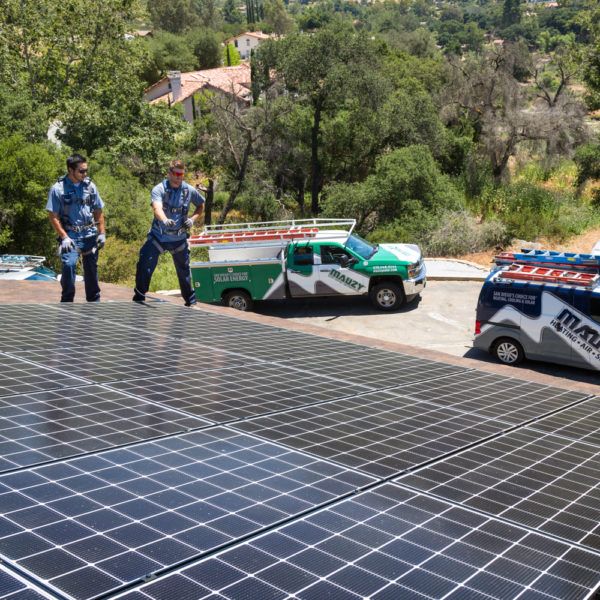 Two Mauzy technicians standing on a roof pointing to a solar panel installation